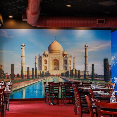 Indian restaurant interior with wooden tables and a Taj Mahal mural.