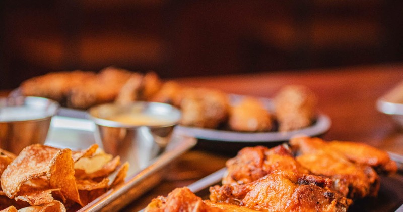 Close-up of a wooden table with a tray of  wings and a platter of crunchy potato chips