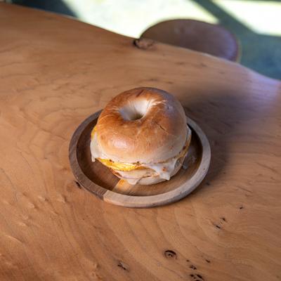 Breakfast bagel with egg and cheese served on a wooden plate.