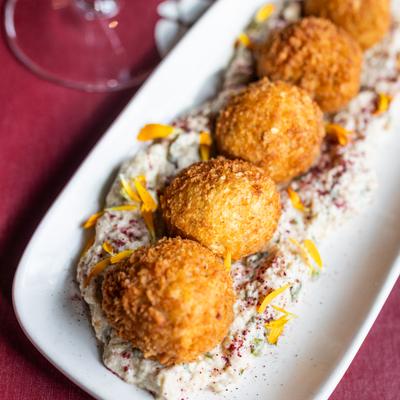 Crunchy cheese and corn croquettes on a rectangular white plate on a burgundy colored menu