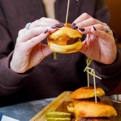 A person holding a small cheeseburger slider.