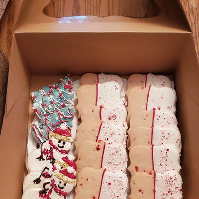 Box of decorated holiday cookies with snowmen, Christmas trees, and rectangular cookies.