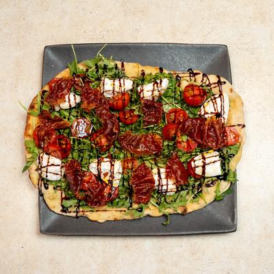 Flatbread topped with arugula, tomatoes, mozzarella, crisp prosciutto, and balsamic drizzle.