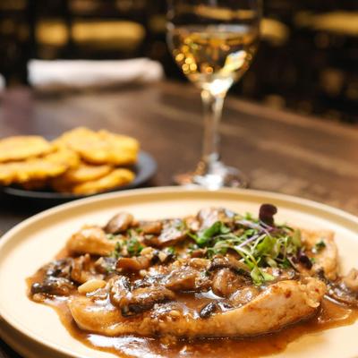 Plate of chicken marsala with mushrooms and microgreens, accompanied with white wine.
