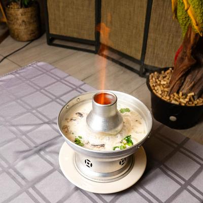 Flaming Thai soup pot with a creamy broth and ingredients, displayed on a checkered tablecloth.