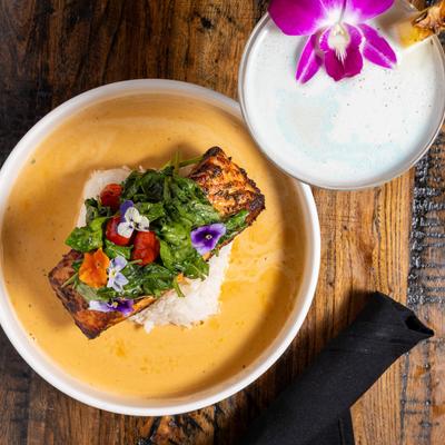 Salmon over rice in a creamy sauce with a cocktail topped with a purple orchid.