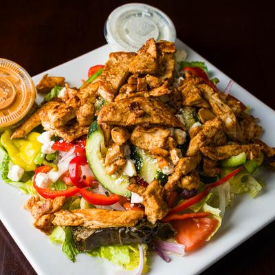 Greek salad with chicken, feta and vegetables, served with dressing on the side.