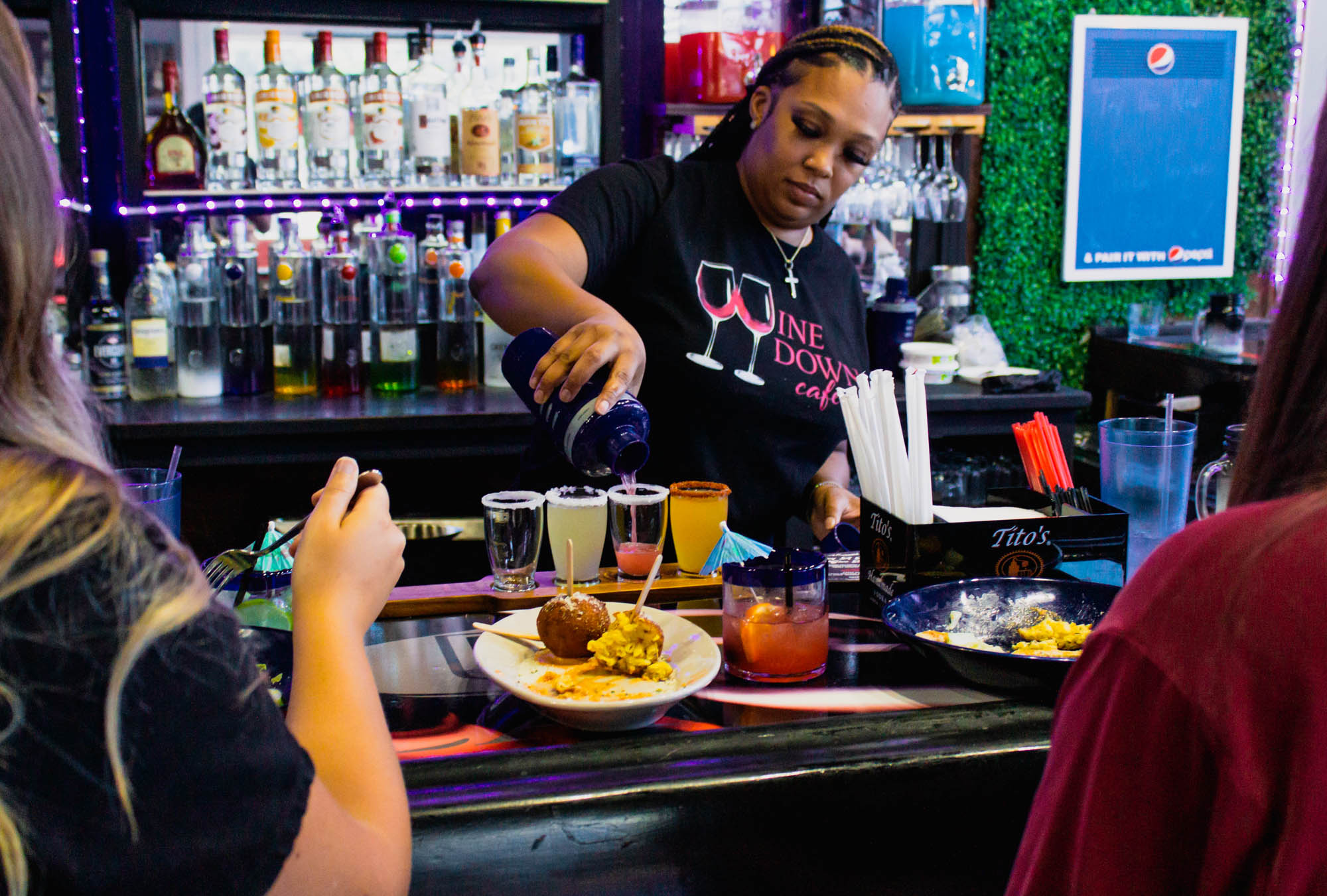 Interior, bar staff pouring a cocktail drink on a cocktail flight behind counter