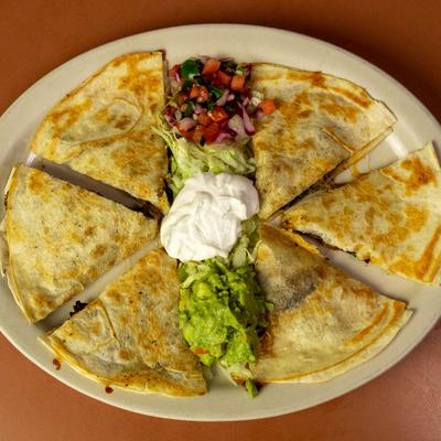 Quesadilla Pastor served on a plate with sour cream, guacamole, and pico de gallo.