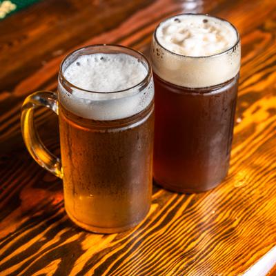 Two draft beers served in glass mugs with frothy heads.