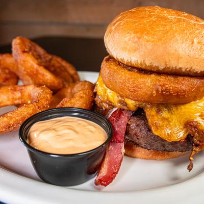 Western burger with cheese, bacon, onion rings and a dipping sauce, close-up.