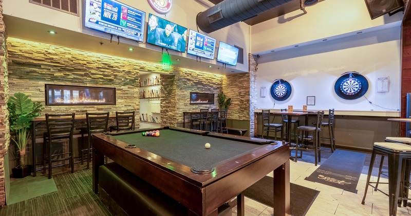 Interior of a modern sports bar, seating area, pool table and two electronic dartboards on the wall