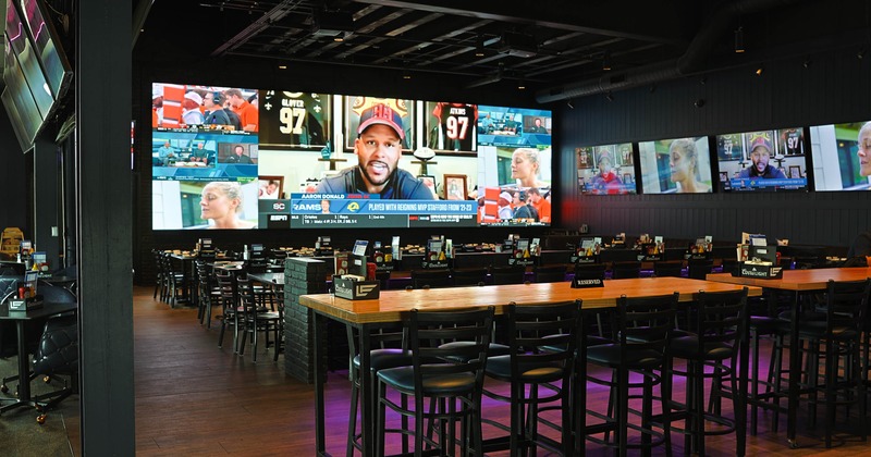 Interior - large screens displaying sports broadcasts; a central communal table with high chairs