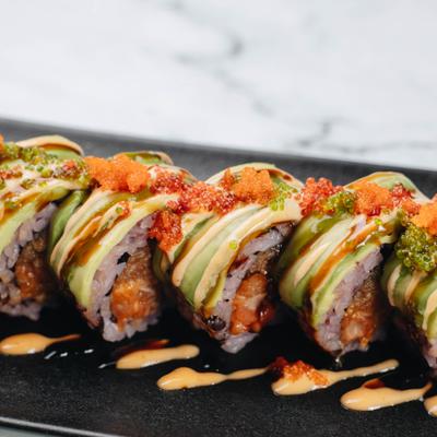 Sushi roll topped with avocado and sauce drizzle.