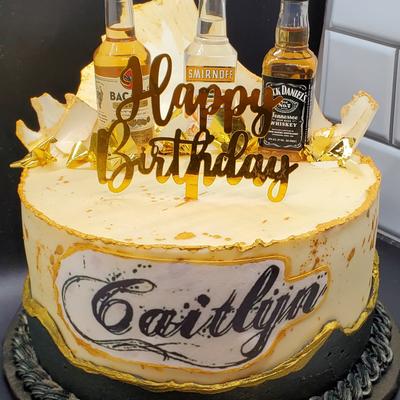 A birthday cake decorated with small bottles of different spirits.