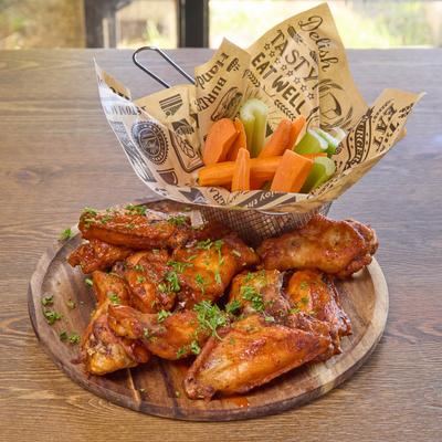 Buffalo Wings served with carrots on a wooden board.