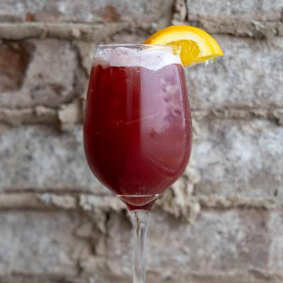 A glass of red sangria, garnished with an orange wedge.