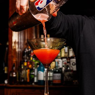 A bartender pours a vibrant pink cocktail into a martini glass.