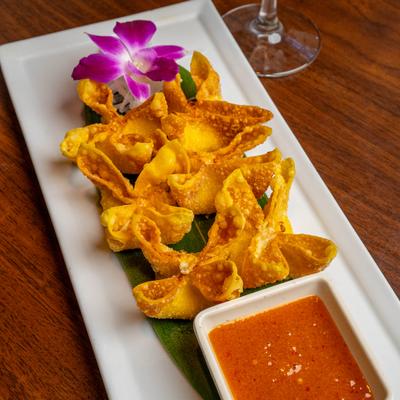 Crab Rangoons served with a dipping sauce and a purple orchid garnish.
