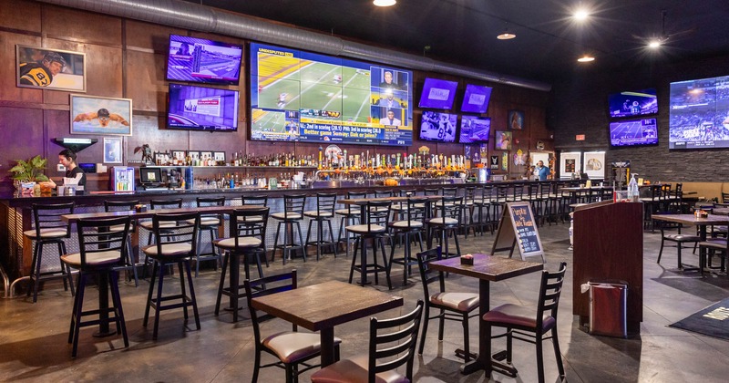 Interior, seating area, large TV panel with many smaller TVs hanged on the wall above the bar