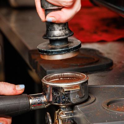 Barista using a coffee tamper and an espresso portafilter to compress and prepare coffee.