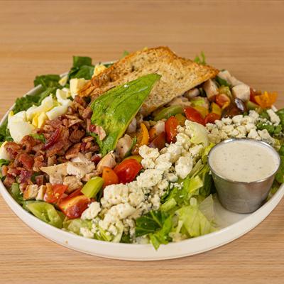 Cobb salad, with bacon, egg, tomato, avocado, chicken, crumbled cheese, lettuce, and crostini.