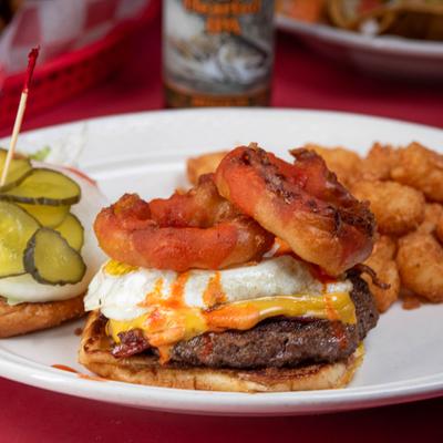Burger topped with fried egg and onion rings, served with tater tots.