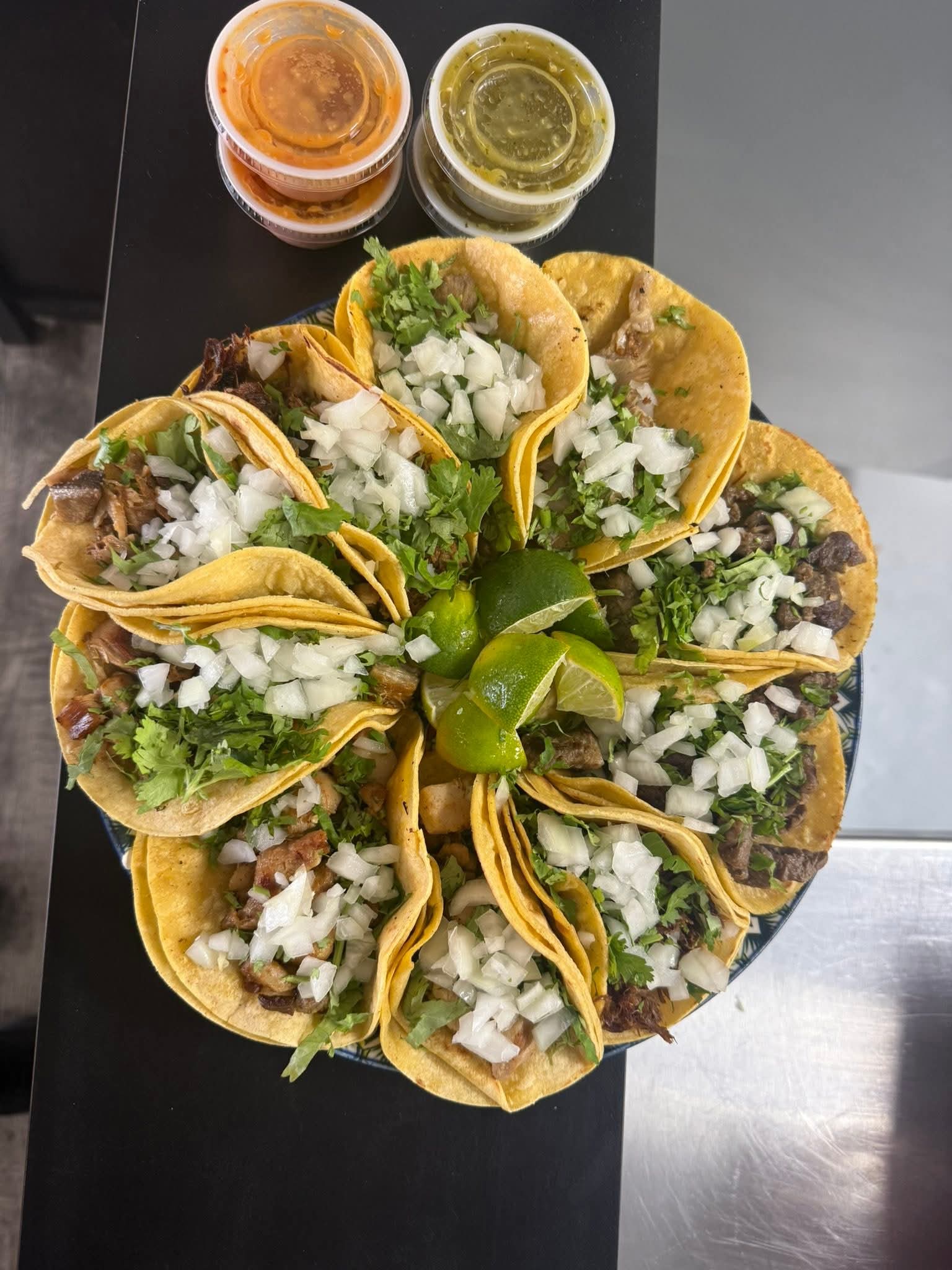 A circular platter of street tacos topped with cilantro, onions, and limes