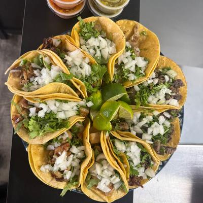 A circular platter of street tacos topped with cilantro, onions, and limes.