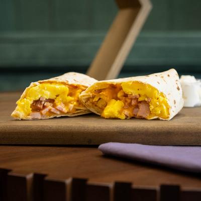 Breakfast burrito rests on a wooden board atop a wooden table with a purple napkin.