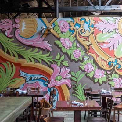 Exterior, mural with colorful swirls, floral patterns, and intricate designs adorns a wall.