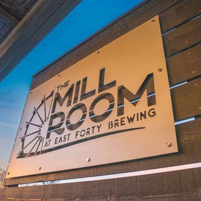 Metal sign with The Mill Room at East Forty Brewing, mounted on a black slat wall.