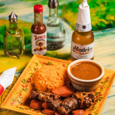 Beef stew with sides of rice and beans, served alongside bottle of beer and condiments.