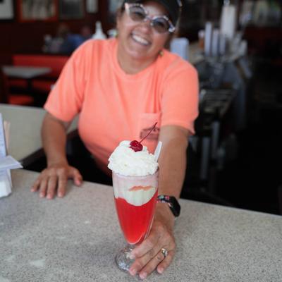 A friendly employee serves Strawberry Sundae on a counter.