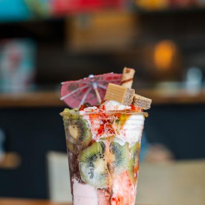 Fruit sunday ice cream cup featuring layers of fruit, wafer stick and a umbrella.