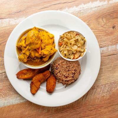 Curried chicken with rice and peas, fried plantains, and stewed cabbage.