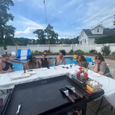 Outdoor hibachi setup by a swimming pool with people seated at a table.