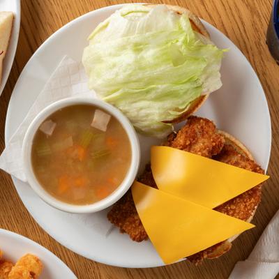 Fried Fish Sandwich topped with cheese and served with a bobl of Bean Soup.