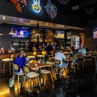 Bar area with a counter, wooden tables, high chairs, neon signs and multiple televisions.