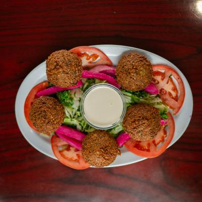 Falafel plate with tomatoes, pickled turnips, salad, and tahini sauce.