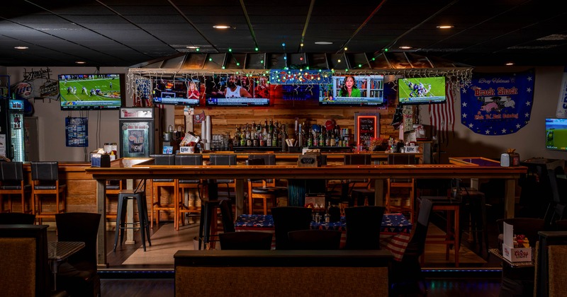 Sports bar interior with a wooden bar, multiple TVs, and festive decor