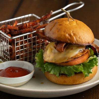 Bacon cheeseburger with lettuce, tomatoes, sweet potato fries, and ketchup.