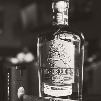 A bottle of bourbon flanked by a cutter and a cigar.