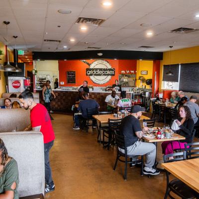 Busy restaurant dining room with guests seated at wooden tables and booth seating.