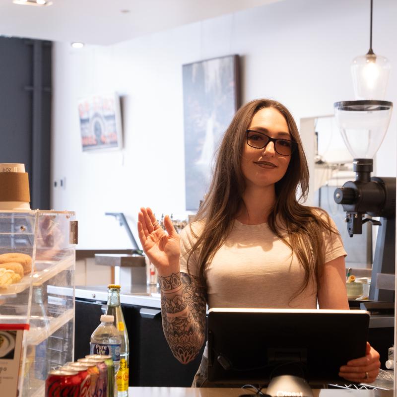 An employee standing behind a barista counter with a cash register.