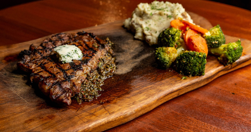 Rib eye served with mashed potatoes and veggies on a wooden board