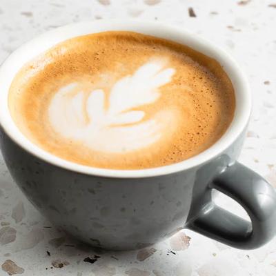 Gray ceramic cup filled with a rich cappuccino sits on a speckled white surface.