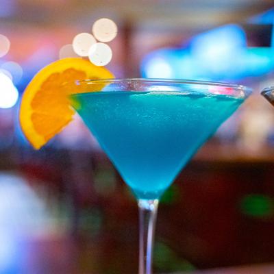 A vibrant blue cocktail served in a martini glass and garnished with an orange slice.