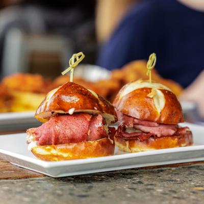 Two small sandwiches with meat and pretzel buns on a white plate.