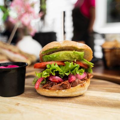 Sandwich with pork, lettuce, tomato, pickled red onion, and avocado.